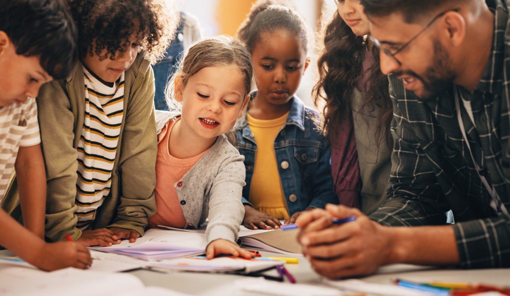 Students doing a creativity project with their teacher in a classroom. Group of primary school children learning how to draw and color with the help of their educator.